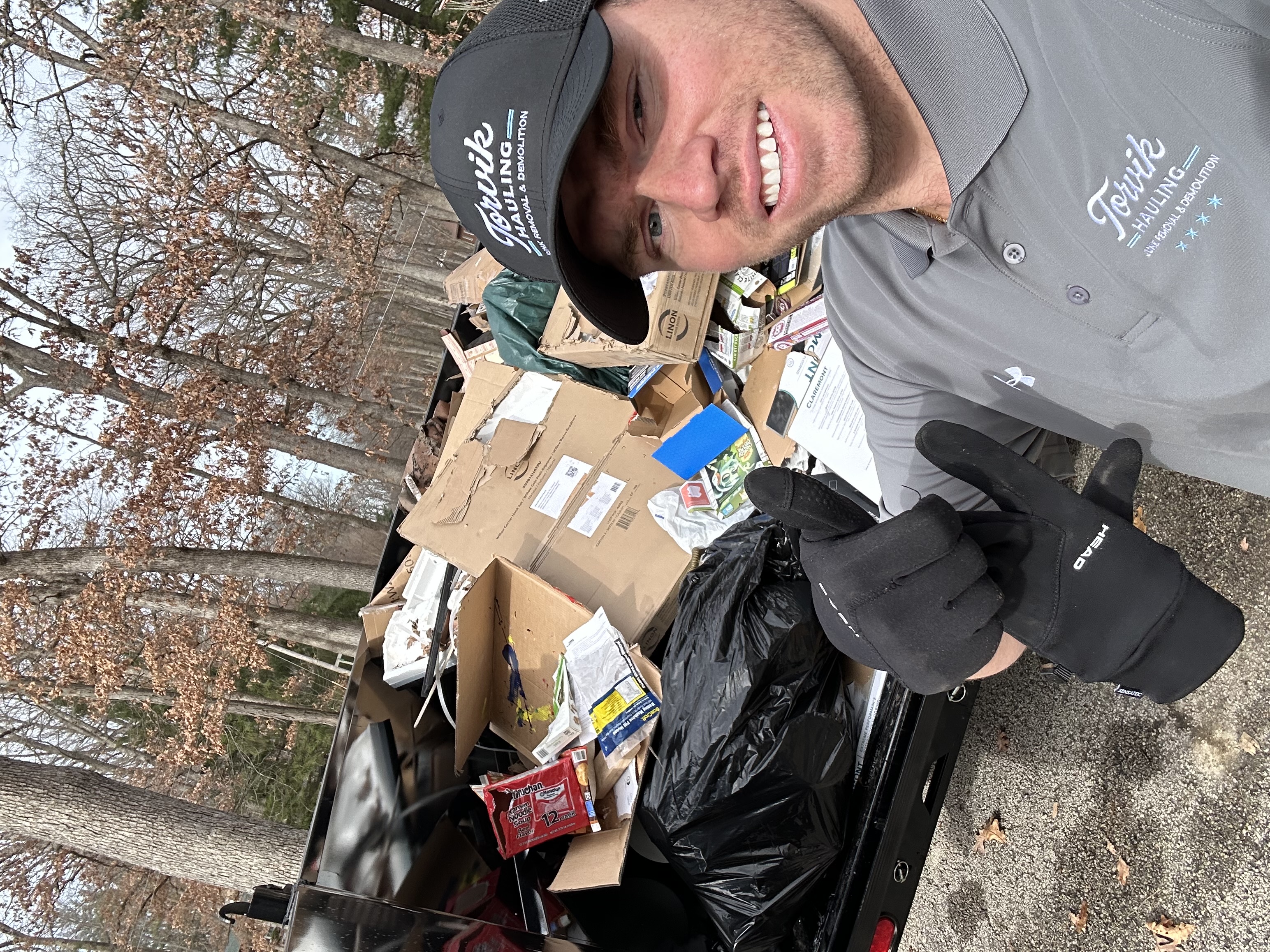 Torvik Hauling owner giving a thumbs-up next to a trailer loaded with boxes, bags, and household junk mid-haul