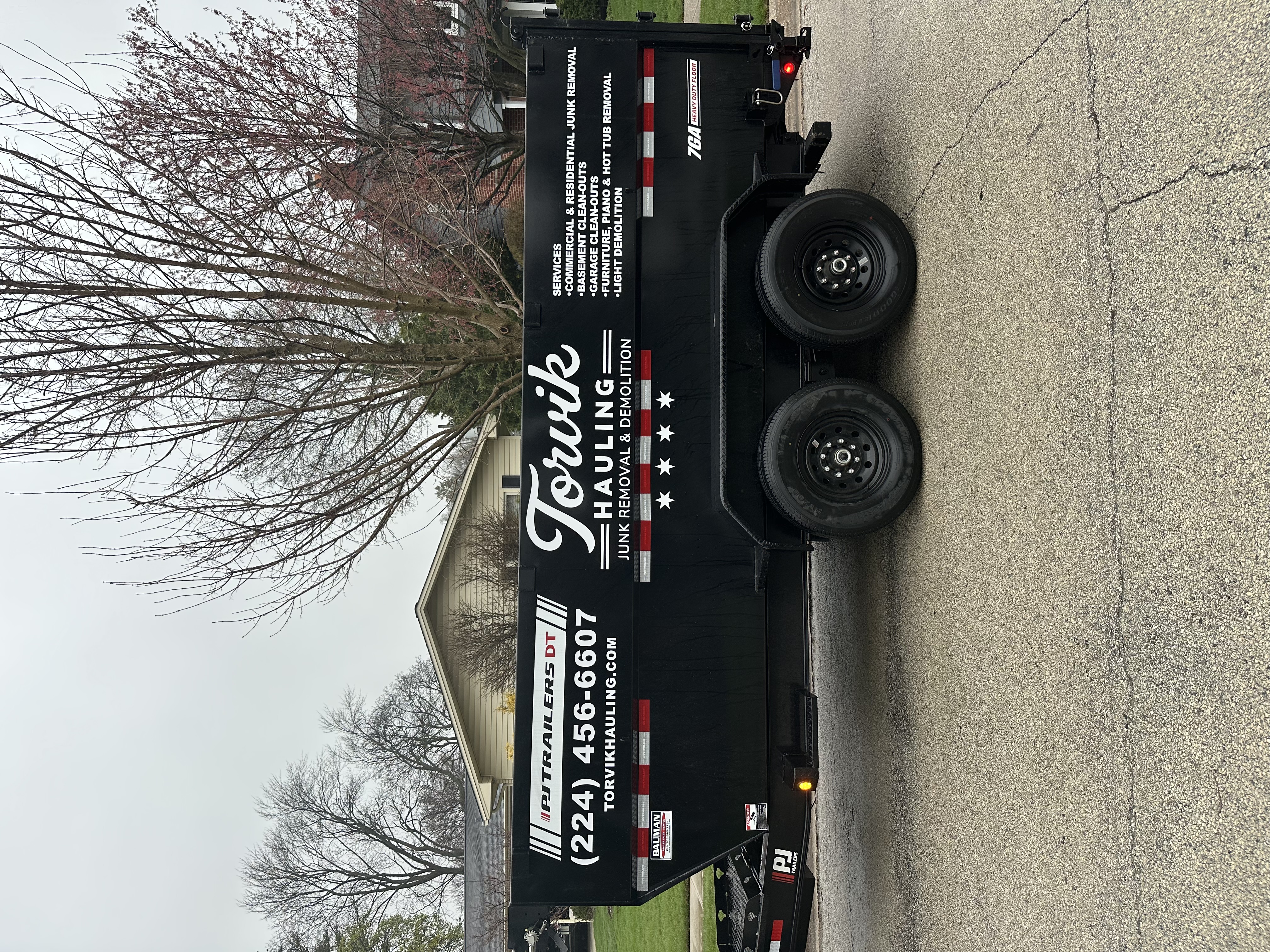 Side view of the Torvik Hauling dump trailer displaying the full services list and phone number (224) 456-6607